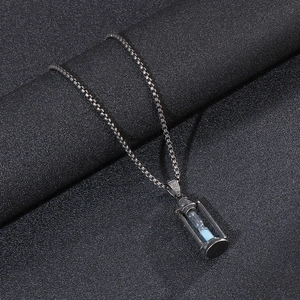 Detailed view of stainless steel hourglass pendant with blue sand on black texture