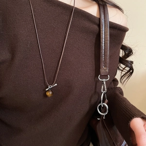 Detail of tiger eye horse pendant necklace worn on a brown sweater for luxury style