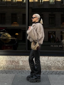 Street style shot of a beige faux fur coat paired with black leather trousers and a shoulder bag