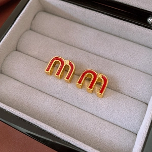 Macro shot of gold-plated red enamel M letter stud earrings in a plush jewelry box