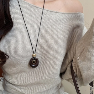 Detail of resin tiger eye oval pendant on a long black cord with a knit sweater