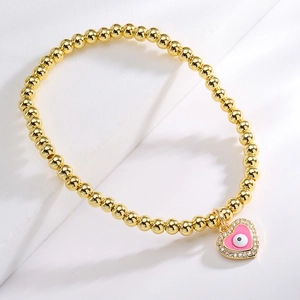 Golden beaded bracelet with a pink heart-shaped evil eye pendant and zircon stones