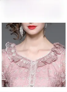 Détail macro du col de robe en dentelle rose avec broderie florale et perles