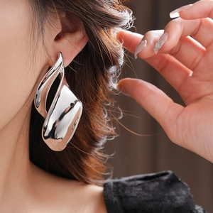 Macro shot of large silver fluid sculpture earrings with a high-shine metallic mirror finish