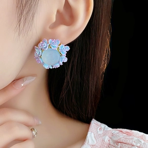 Close-up of a floral stud earring featuring a light blue stone and purple petals