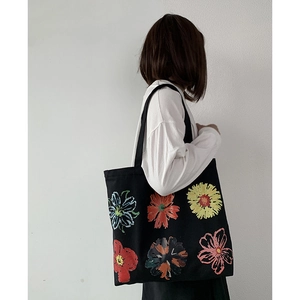 Shoulder view of a black floral canvas tote bag featuring colorful hand-painted flowers