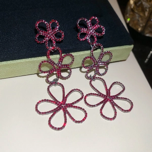 Close-up of silver-tone floral drop earrings with red rhinestones and hollow design