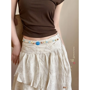 Détail d'une chaîne de taille bohème avec perle en résine bleue sur une robe blanche