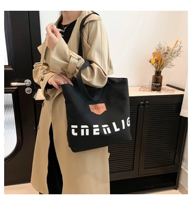 Detailed shot of large black canvas tote bag with white lettering and brown leather logo