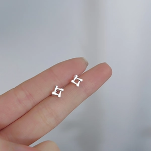 Macro view of geometric silver cross earrings held on a fingertip for size comparison