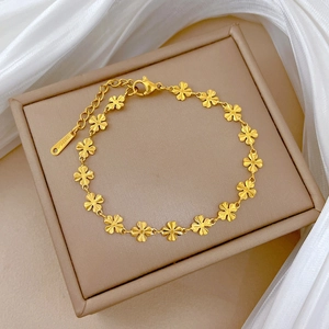 Detailed close-up of golden stainless steel clover chain bracelet on a leather box