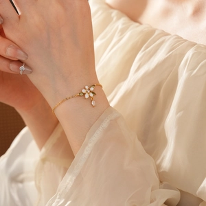 Dettaglio di un bracciale dorato con fiore in smalto bianco e ciondoli a foglia verde