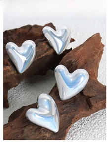 Macro shot of 3D heart-shaped silver earrings with high-gloss metallic finish on dry wood