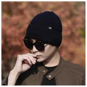 Detail of dark blue ribbed knit beanie featuring a rectangular silver metal logo plate