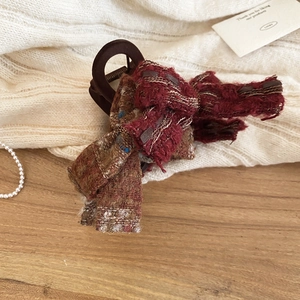 Detail of burgundy checkered tweed bow hair claw clip on cozy white knit background