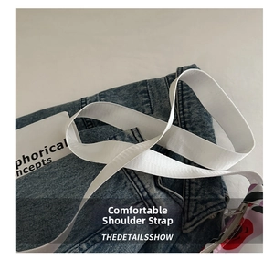 Close-up of white woven shoulder strap with floral zipper pouch on denim fabric
