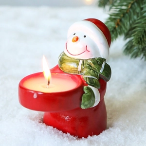 Christmas snowman ceramic candle holder with burning tealight on snowy winter background