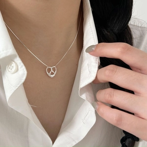 Detail shot of a silver knotted heart pendant on a fine chain worn with a white shirt