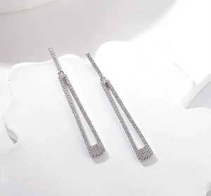 Macro shot of silver geometric tassel earrings with zircon inlay on white marble