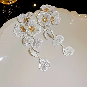 Macro detail of white flower petal earrings with gold stamen and elegant long tassels
