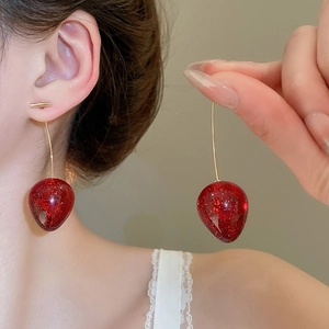 Détail macro d'une boucle d'oreille fraise rouge pailletée sur modèle avec crochet doré