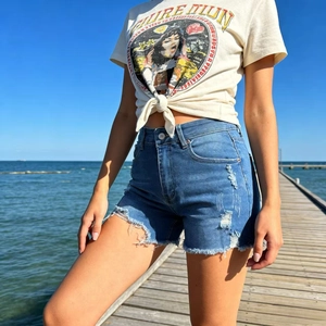 Detail of high waisted distressed denim shorts with frayed hems and Pure Luck graphic t-shirt