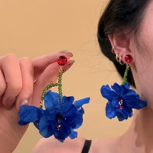Bohemian floral dangle earrings with blue silk flowers and green beads on model