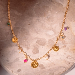 Gold necklace with freshwater pearls, colorful zircons and embossed coin pendant on marble