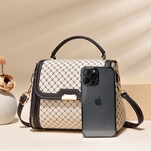 Fashionable beige crossbody bag with brown pattern and leather handles beside a phone