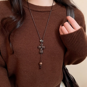 Gros plan d'un collier croix léopard sur pull marron au style esthétique vintage minimaliste