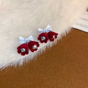 Close-up of Christmas earrings with red flocked bells, white bows and pearls on plush