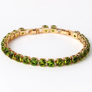 Close-up of golden tennis bracelet featuring round green stones in square settings