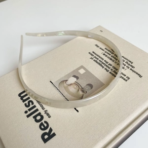 Detail van een parelwitte acetaat hoofdband rustend op een boek met elegante afwerking