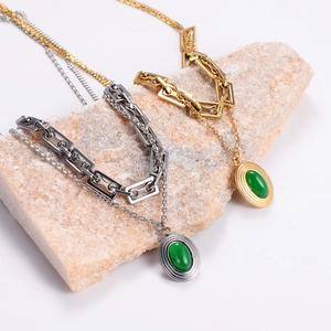 Detail of layered gold and silver necklaces with green emerald pendants on a natural stone