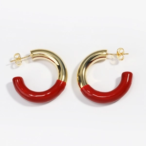 Détail de boucles d'oreilles dorées en C avec finition émail rouge sur fond blanc