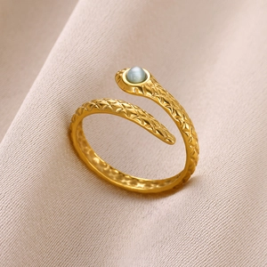 Macro shot of gold snake ring with a blue gemstone head on beige silk fabric
