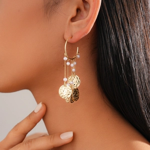 Detail view of gold hoop tassel earrings with white pearls and hammered metal discs on model