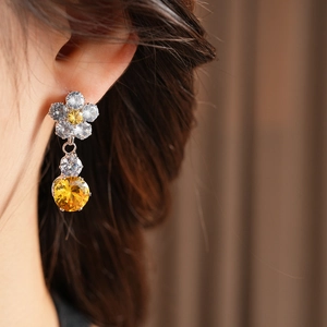 Detail of zircon flower drop earrings with a yellow round gemstone on a model