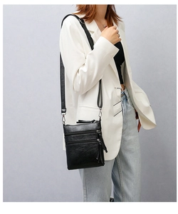 Detail view of black crossbody phone bag showing triple zipper compartments and long tassels