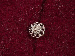 Gros plan sur un bouton fleur en métal argenté sur un tissu en tweed bordeaux