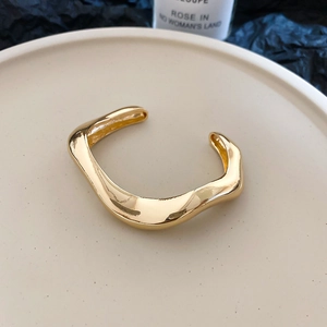 Detailed close-up of golden irregular wavy open bracelet on minimalist ceramic plate