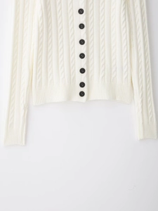 Detailed cable-knit texture on white cardigan featuring contrasting black buttons