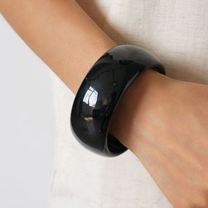 Macro shot of wide black acrylic bangle with polished mirror finish on a person wrist