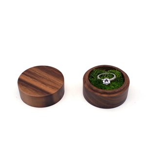 Detail view of round walnut ring box with green moss lining and a silver diamond ring