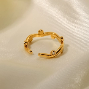 Close-up of 18K gold plated leaf-shaped open ring with white diamond inlay on beige cloth