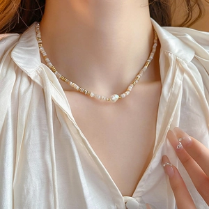 Close-up of gold-plated necklace featuring baroque pearl and shell beads on a model