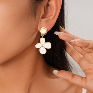 Close-up of elegant gold flower earrings with white enamel worn by a model