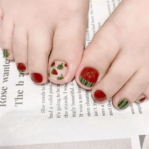 Close-up of red and green watermelon themed press-on toenails on a newspaper background