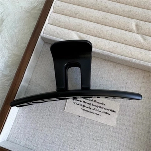 Close-up of a large black hair claw clip presented in a premium wooden jewelry box