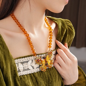 Detail of vintage gold butterfly pendant with amber crystals on beaded sweater necklace